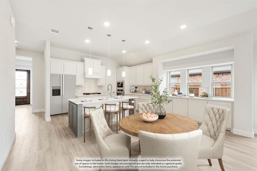 Open-concept kitchen and dining area with white cabinets, gray island, pendant lights, and round wood dining table