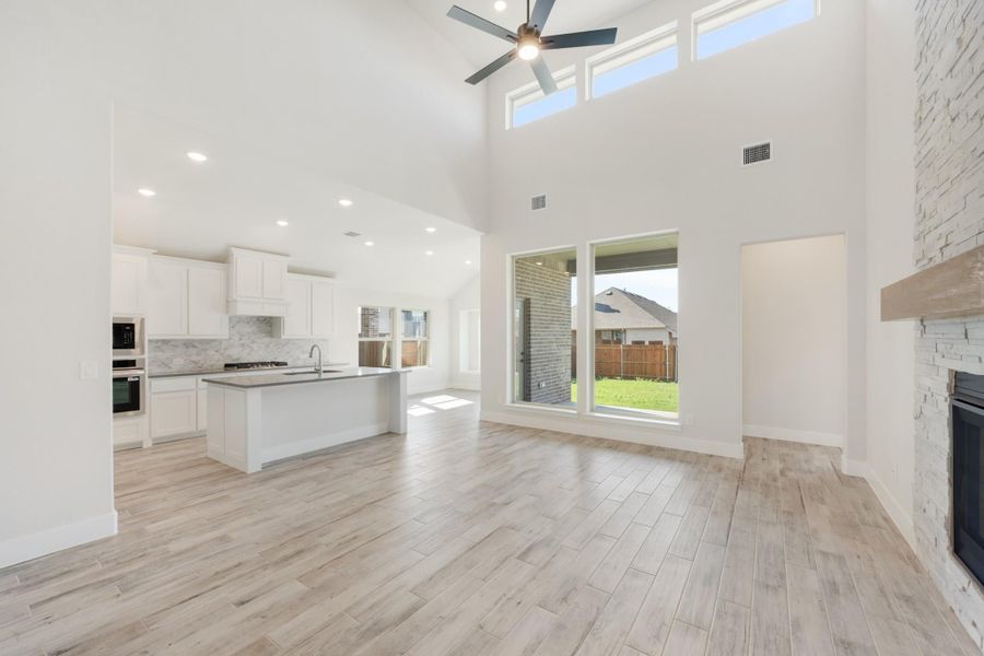 Open living area with high ceilings, stone fireplace, and kitchen with white cabinets and island Open living area with high ceilings, stone fireplace, and kitchen with white cabinets and island
