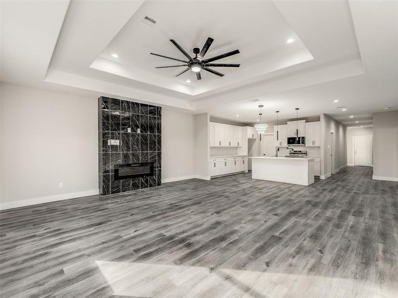 Unfurnished living room featuring a fireplace, light wood-type flooring, a tray ceiling, and ceiling fan