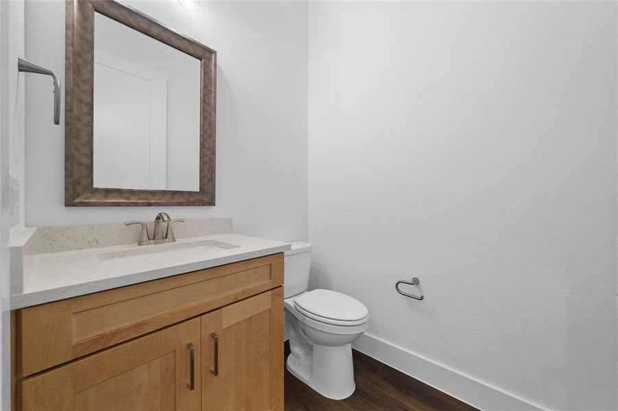 Powder room featuring a single-sink vanity with light wood cabinetry and a light-toned countertop, a brushed nickel faucet, and a framed mirror