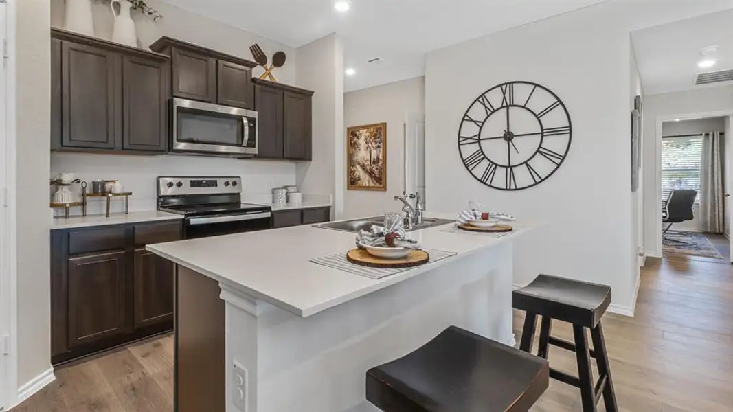 Kitchen featuring dark wood finish cabinetry, stainless steel appliances, an island with sink, a kitchen bar, and light wood-type flooring