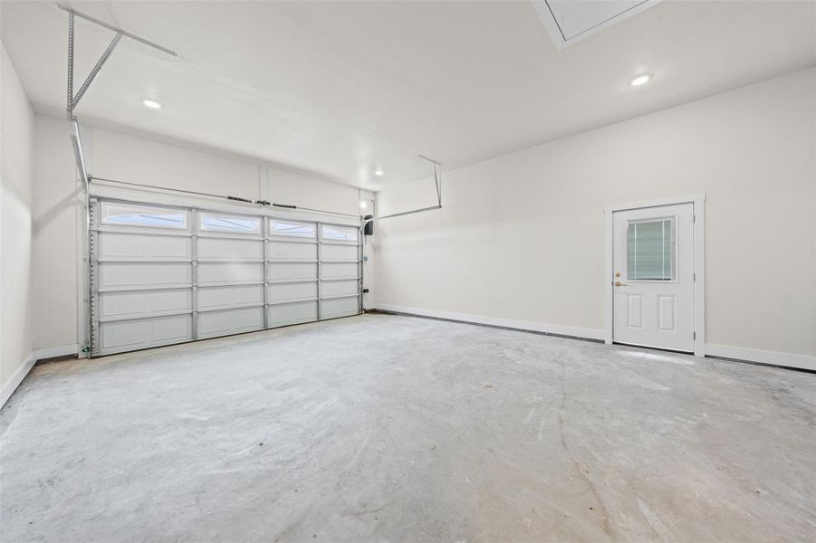A spacious garage features durable concrete flooring, recessed lighting, and a modern garage door.