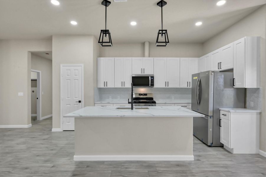 Gourmet kitchen view featuring stainless steel appliances, a deep undermount sink with a high-neck faucet, and beautiful stone-patterned countertops.