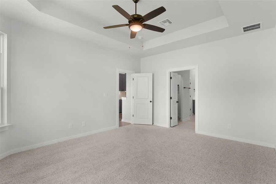 Unfurnished bedroom featuring a tray ceiling, light carpet, and a ceiling fan Unfurnished bedroom featuring a tray ceiling, light carpet, and a ceiling fan