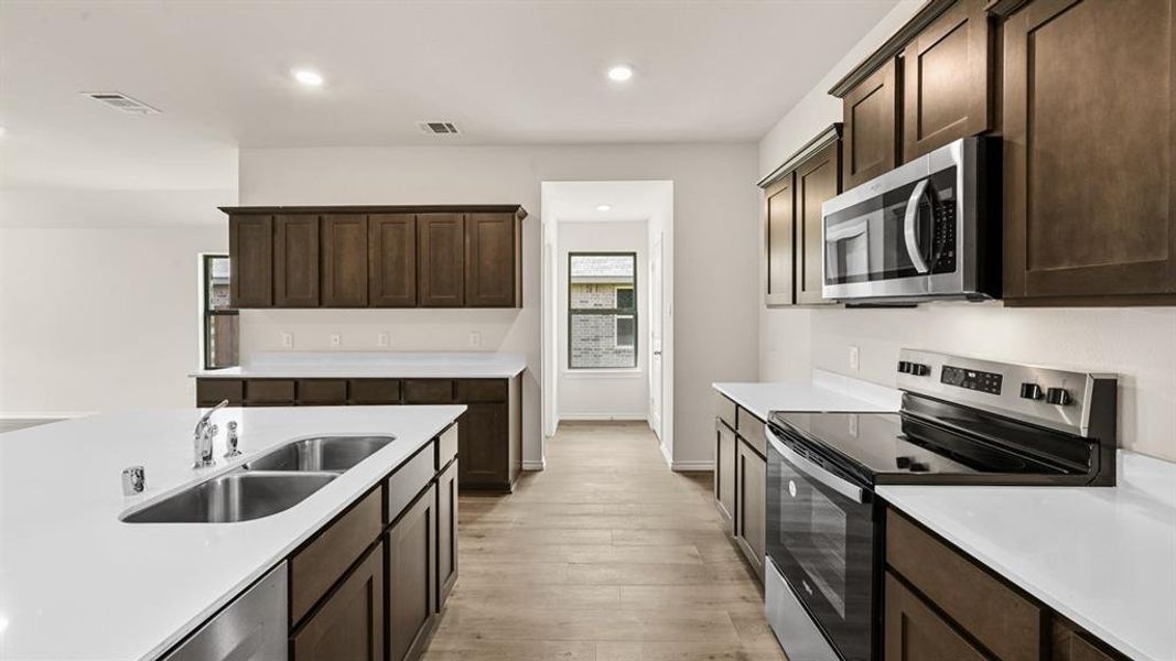 Kitchen featuring dark wood cabinetry, white countertops, stainless steel appliances, and wood-finish flooring Kitchen featuring dark wood cabinetry, white countertops, stainless steel appliances, and wood-finish flooring