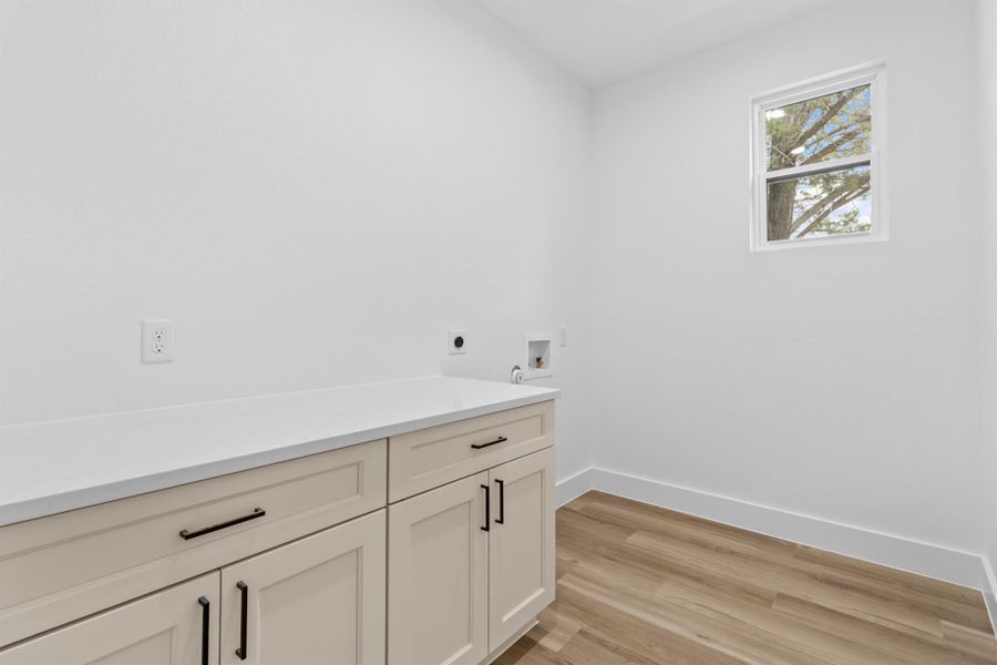 Laundry room with light wood-style flooring, hookup for a washing machine, hookup for an electric dryer, cabinet space, and quartz countertop