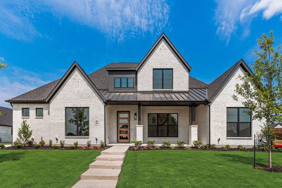 View of front facade featuring a porch, a front yard, a standing seam roof, brick siding, and a metal roof