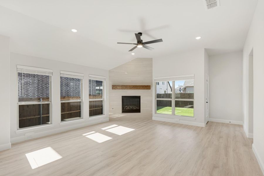 Open living room with light wood floors, tile fireplace, ceiling fan, and large windows