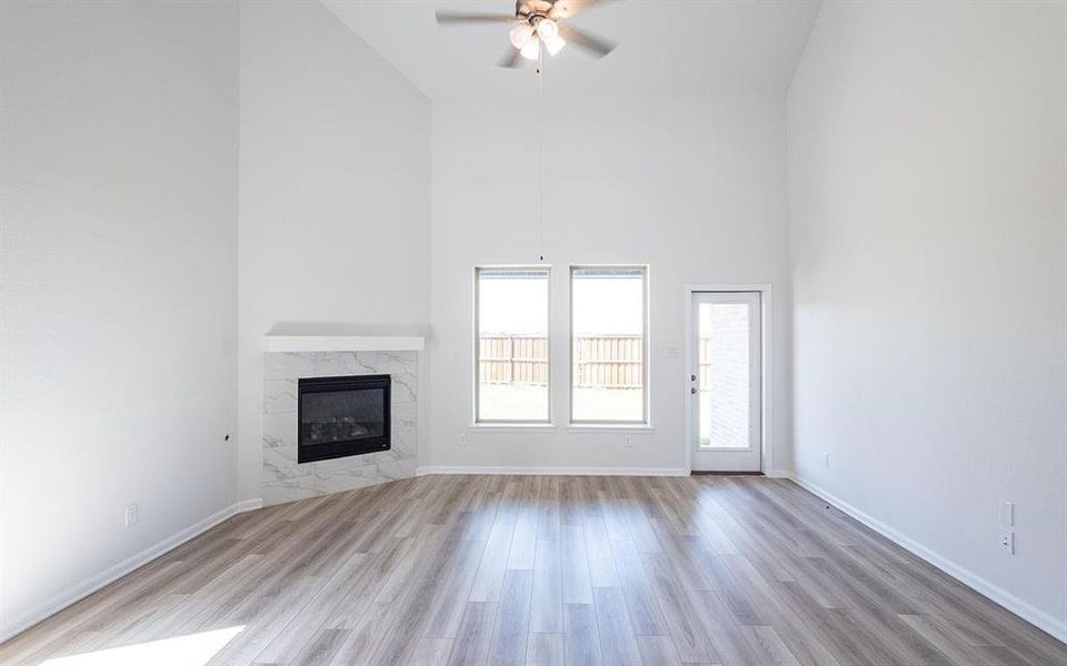 Unfurnished living room featuring light wood-type flooring, ceiling fan, a towering ceiling, and a fireplace