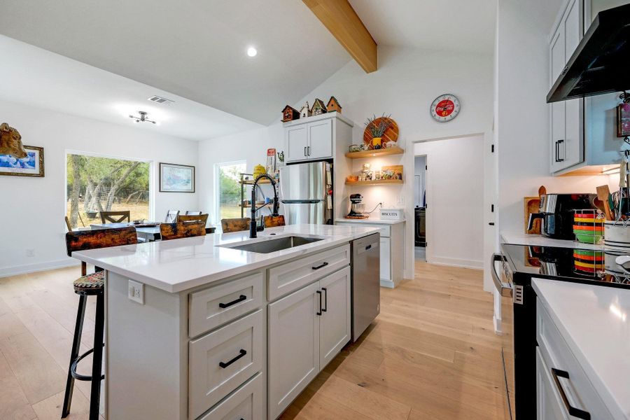 Kitchen featuring light wood-style floors, a breakfast bar area, stainless steel appliances, a center island with sink, and white cabinets