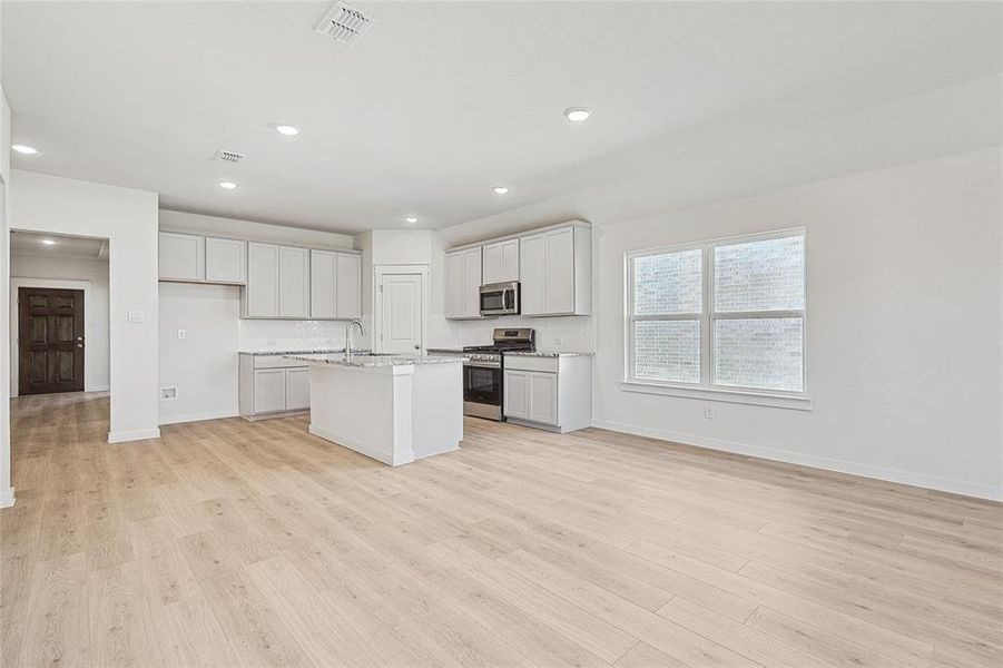 Kitchen with stainless steel appliances, light stone counters, light wood-type flooring, and a kitchen island with sink