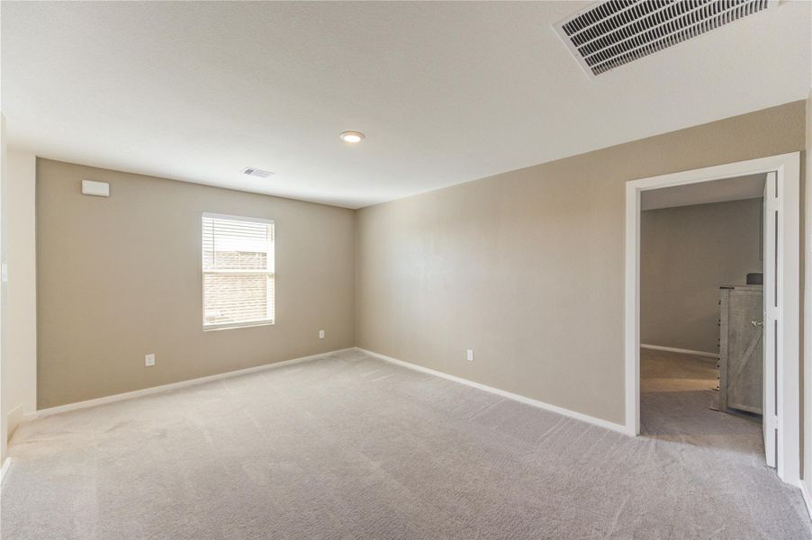 This photo shows a spacious, carpeted room with neutral walls and a ceiling light. There's a window allowing natural light, and an open doorway leading to another room, ideal for a cozy living space or bedroom.