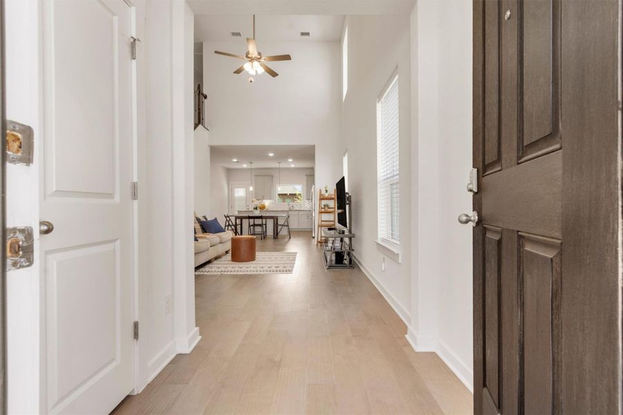 Bright and welcoming entryway leads to an open-concept living area with high ceilings, a ceiling fan, and hardwood floors. The space flows into a modern kitchen and dining area, perfect for entertaining.