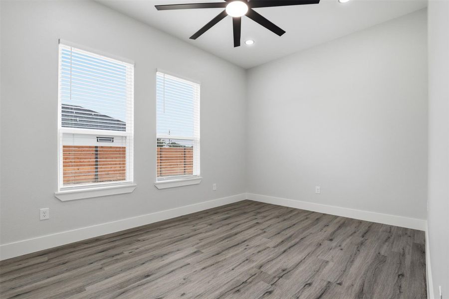 Room featuring wood-finish flooring, light gray walls, and two windows with blinds