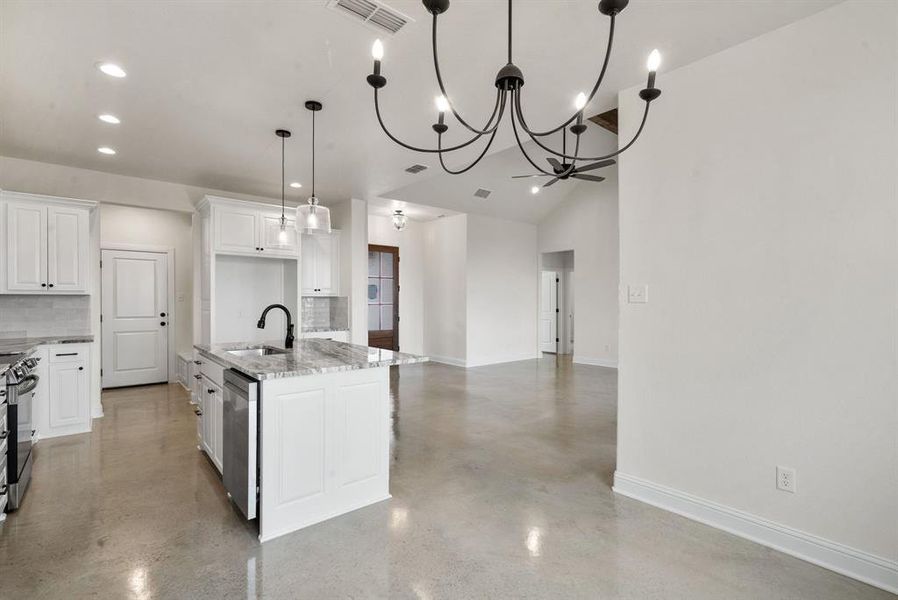 Kitchen with light stone counters, white cabinets, sink, tasteful backsplash, and a kitchen island with sink