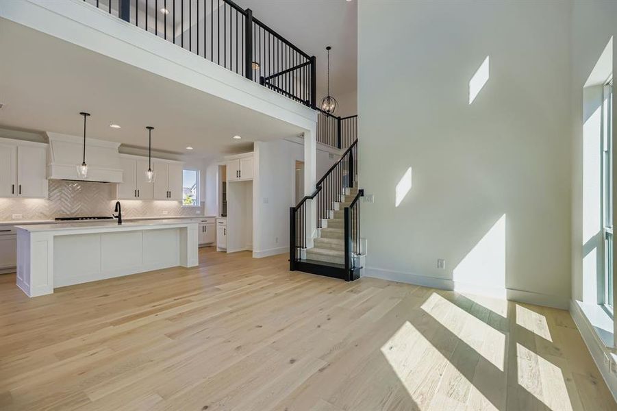 Unfurnished living room featuring stairs, light wood finished floors, and a towering ceiling Unfurnished living room featuring stairs, light wood finished floors, and a towering ceiling