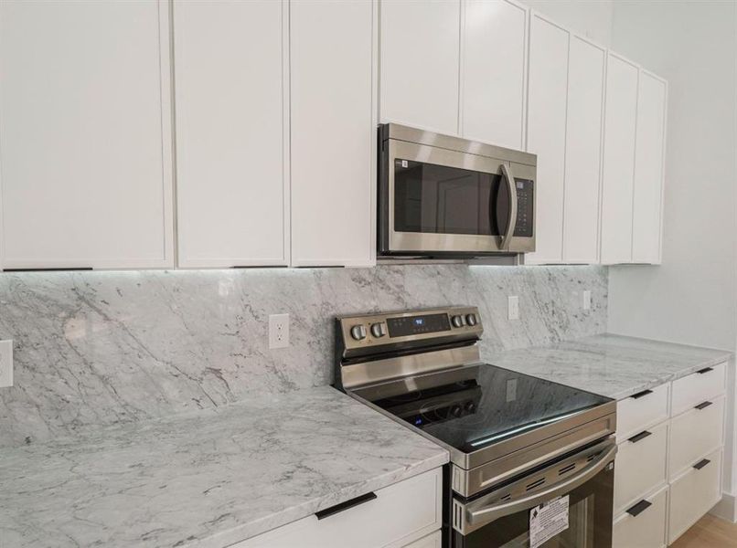 Kitchen with stainless steel appliances, white cabinets, light stone countertops, decorative backsplash, and modern cabinets Kitchen with stainless steel appliances, white cabinets, light stone countertops, decorative backsplash, and modern cabinets