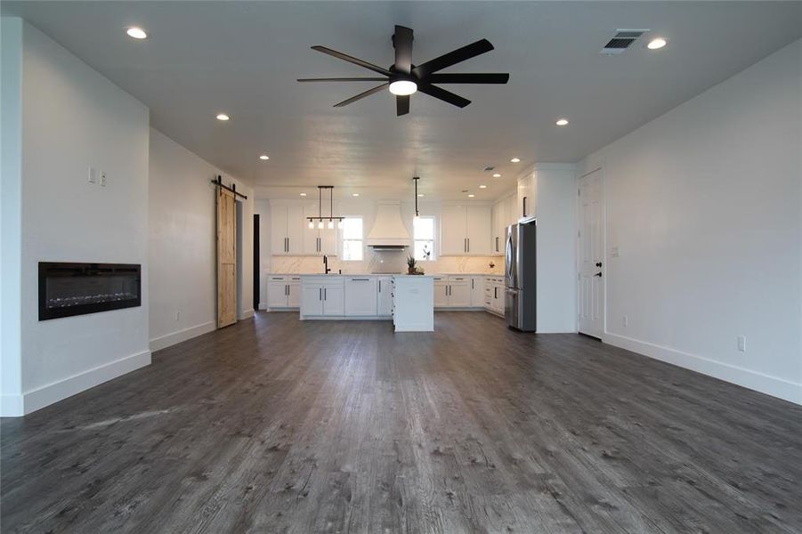 Unfurnished living room featuring a barn door, ceiling fan, dark wood-type flooring, and recessed lighting Unfurnished living room featuring a barn door, ceiling fan, dark wood-type flooring, and recessed lighting