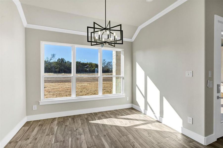 Unfurnished dining area with vaulted ceiling, crown molding, a chandelier, and light hardwood / wood-style floors