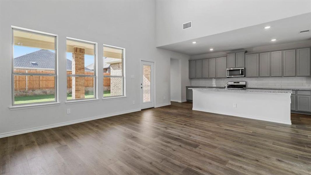 Kitchen featuring gray cabinetry, an island with sink, decorative backsplash, dark wood finished floors, and recessed lighting