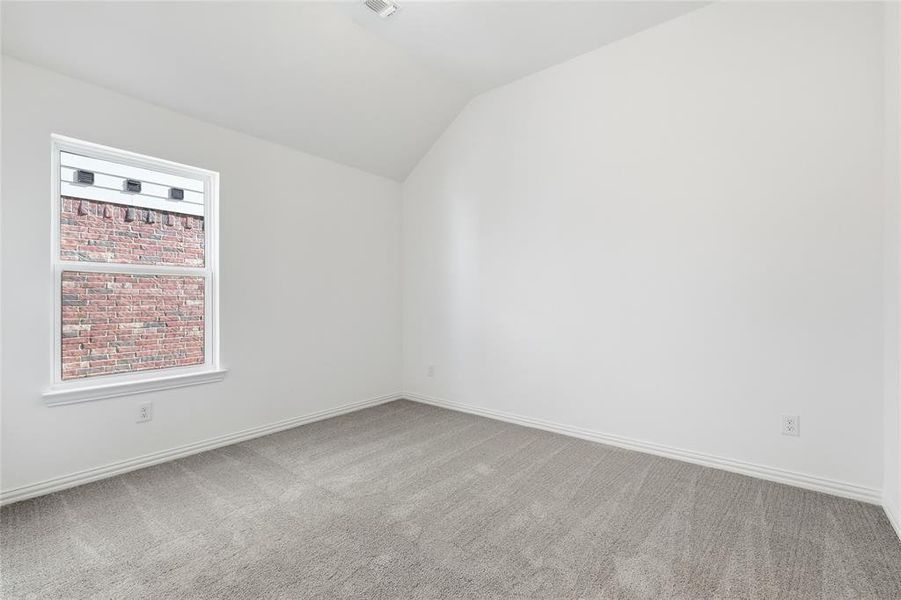 Vaulted ceiling room with neutral carpet flooring, crisp white walls, and a large window featuring white trim