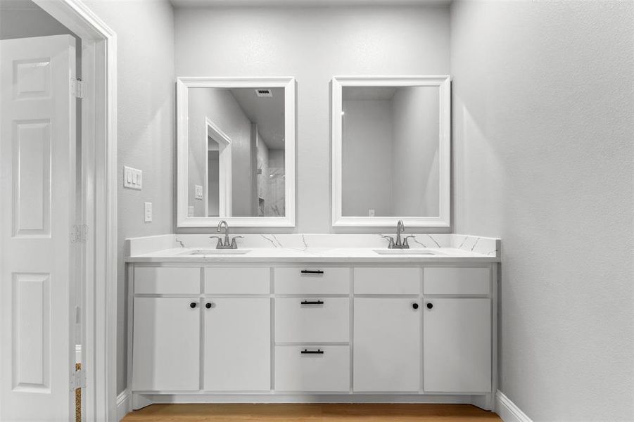 Full bathroom with double vanity, a textured wall, and light wood-type flooring