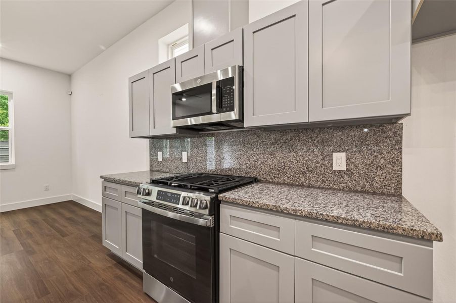 Modern kitchen with sleek gray cabinets, stainless steel appliances, and a granite countertop. The room features a gas stove and microwave, with ample storage and a warm wood floor. Modern kitchen with sleek gray cabinets, stainless steel appliances, and a granite countertop. The room features a gas stove and microwave, with ample storage and a warm wood floor.