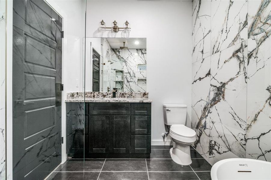 Bathroom with toilet, tile walls, tile patterned flooring, a bathing tub, and vanity