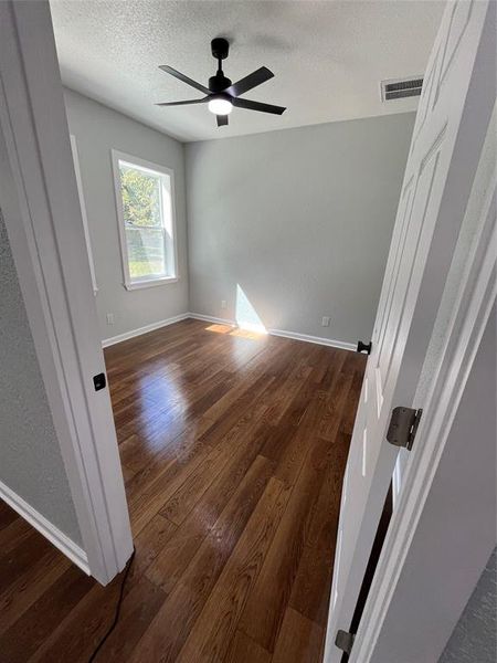 Unfurnished room with dark wood-style floors, a textured ceiling, a textured wall, and a ceiling fan Unfurnished room with dark wood-style floors, a textured ceiling, a textured wall, and a ceiling fan