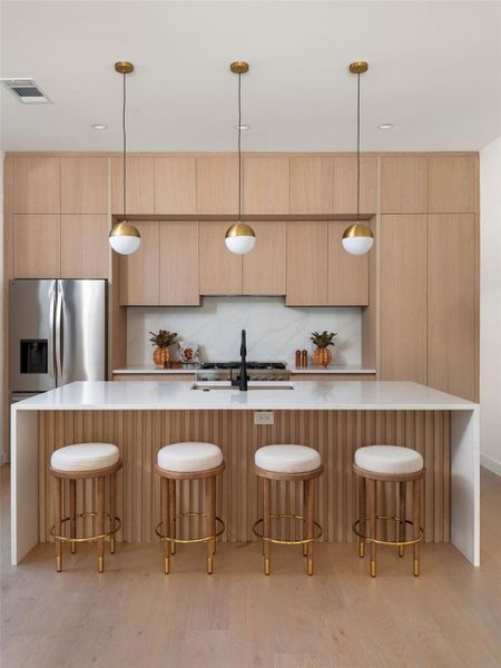 Kitchen with light wood-style floors, modern cabinets, light stone counters, and a large island with sink