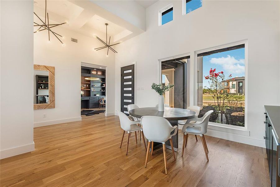 Expansive dining area featuring high ceilings, wood-finish flooring, two modern linear chandeliers, and large windows with transom lighting Expansive dining area featuring high ceilings, wood-finish flooring, two modern linear chandeliers, and large windows with transom lighting