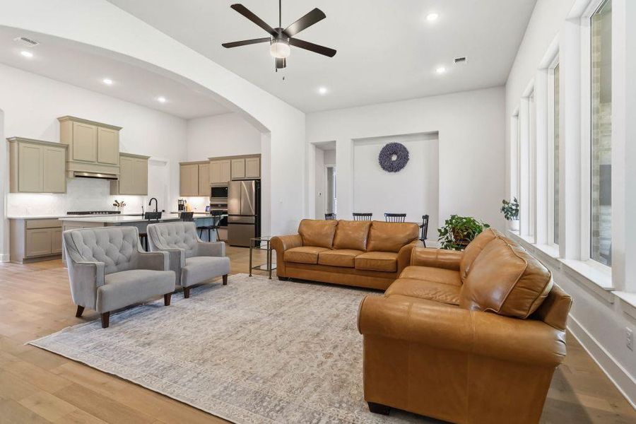 An inviting open-concept living space features light wood flooring, an elegant ceiling fan, and recessed lighting throughout.