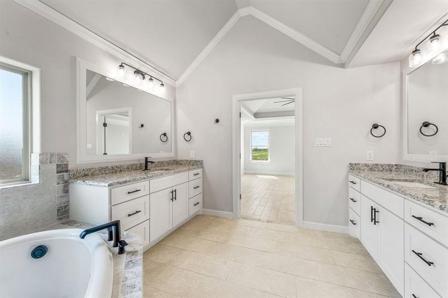 Bathroom featuring ornamental molding, vaulted ceiling, two vanities, a garden tub, and light tile patterned floors