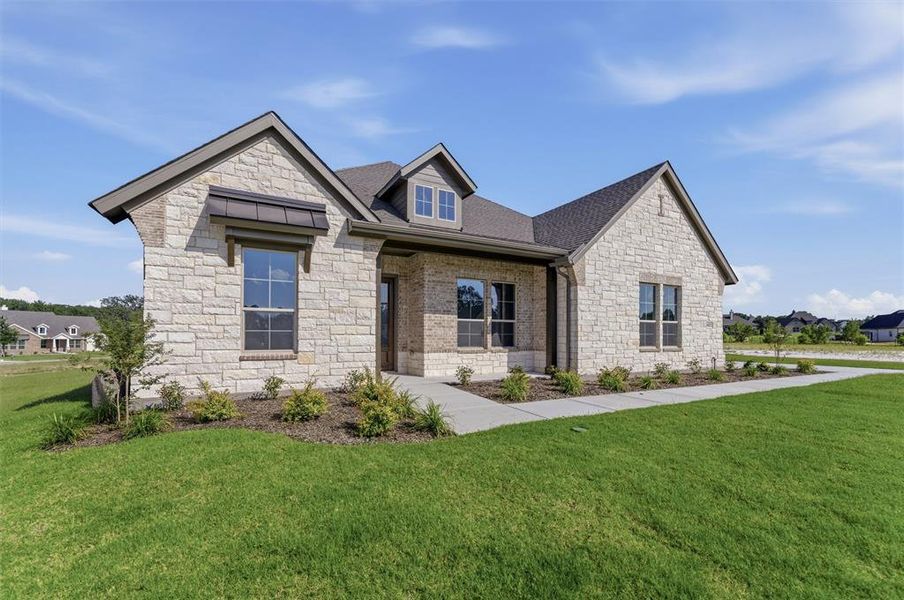 Stone facade residence featuring a dark shingle roof, a front dormer window, and mature landscaping Stone facade residence featuring a dark shingle roof, a front dormer window, and mature landscaping