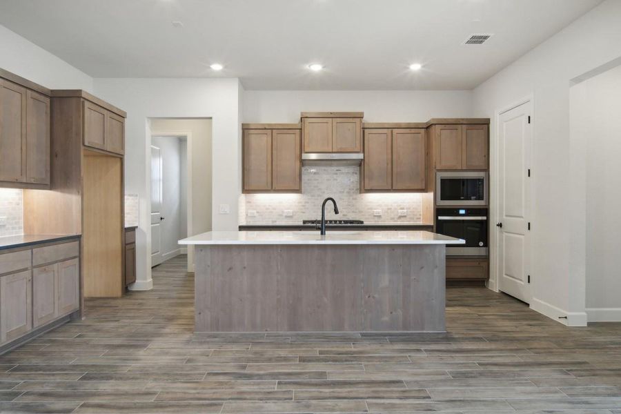 Kitchen featuring tasteful backsplash, wood finished floors, under cabinet range hood, stainless steel appliances, and visible vents Kitchen featuring tasteful backsplash, wood finished floors, under cabinet range hood, stainless steel appliances, and visible vents