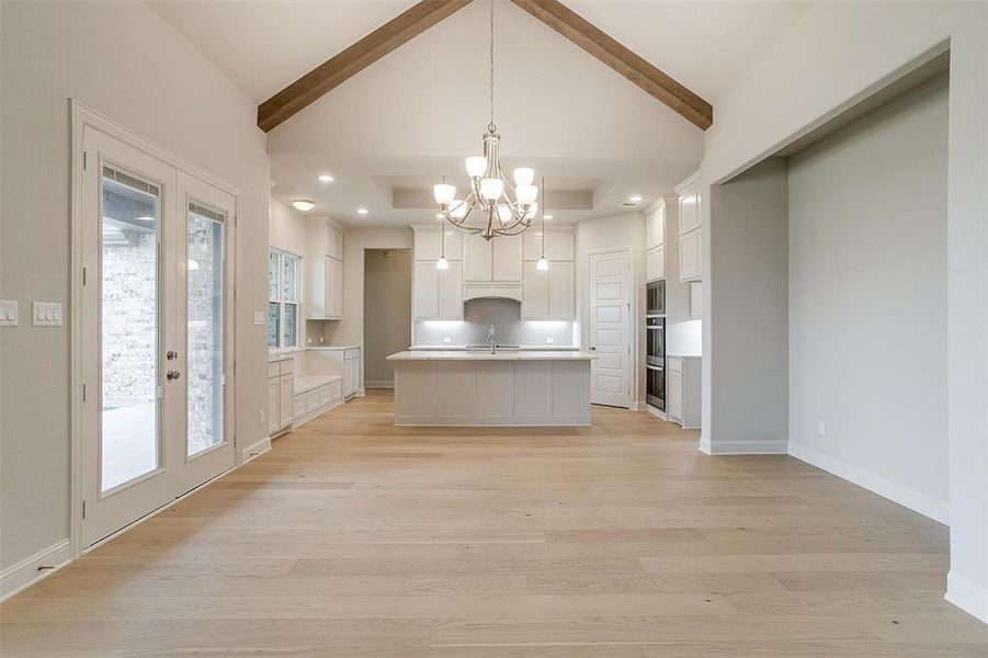 Kitchen with white cabinetry, a kitchen island with sink, light hardwood / wood-style floors, decorative backsplash, and decorative light fixtures