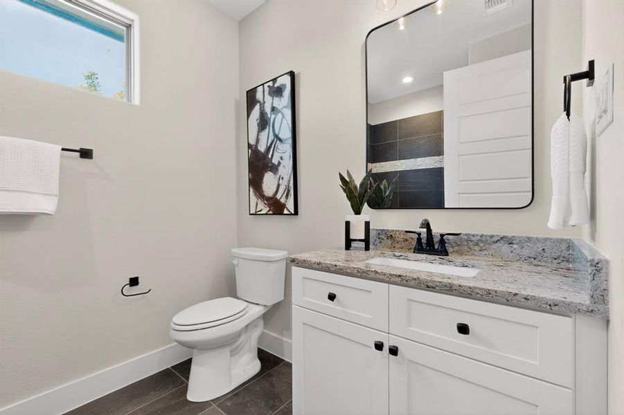 Bathroom featuring a single vanity with stone countertop, white cabinetry, dark plumbing fixtures, and dark tile flooring