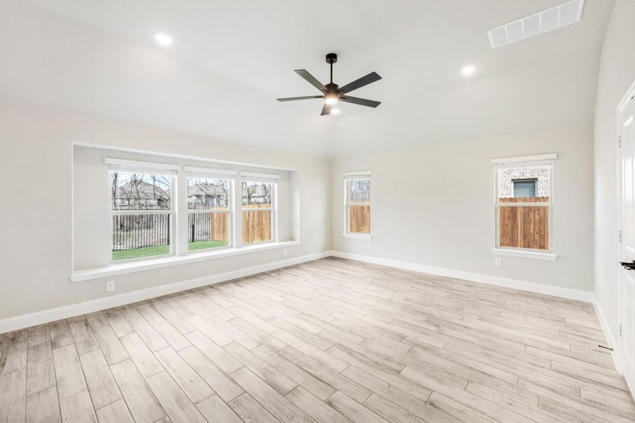 Empty room with light wood floors, ceiling fan, and multiple windows with backyard views