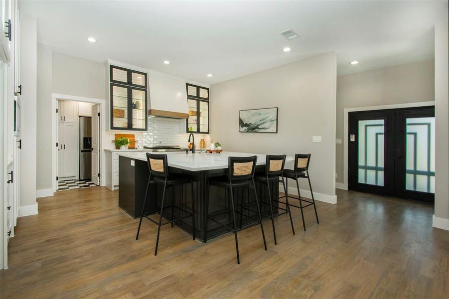 Kitchen with a breakfast bar area, decorative backsplash, dark hardwood / wood-style floors, and a kitchen island with sink