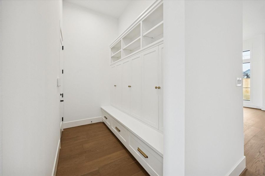 Custom mudroom with built in cabinetry, upper cubbies, and a bench seat with integrated storage keeps everyday essentials organized and out of sight. Wide plank hardwood floors and brushed brass hardware elevate the clean, functional design with a polished finish.