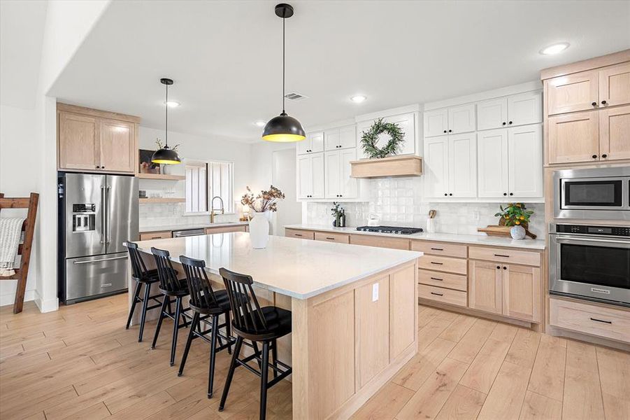 Kitchen with pendant lighting, a center island, decorative backsplash, light hardwood / wood-style floors, and stainless steel appliances