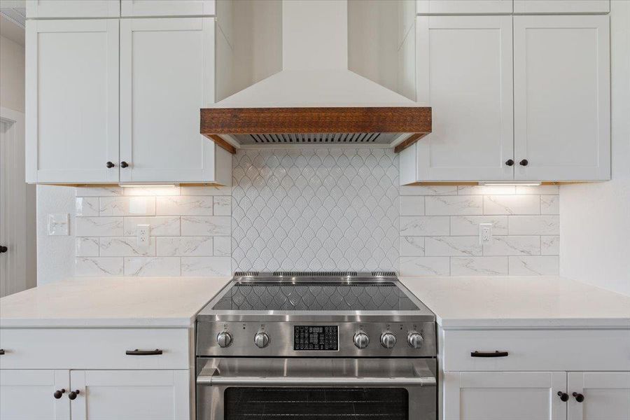 A refined kitchen showcases crisp white cabinetry, marble-style subway tile, and a modern stainless steel range with a decorative wood-trimmed hood.