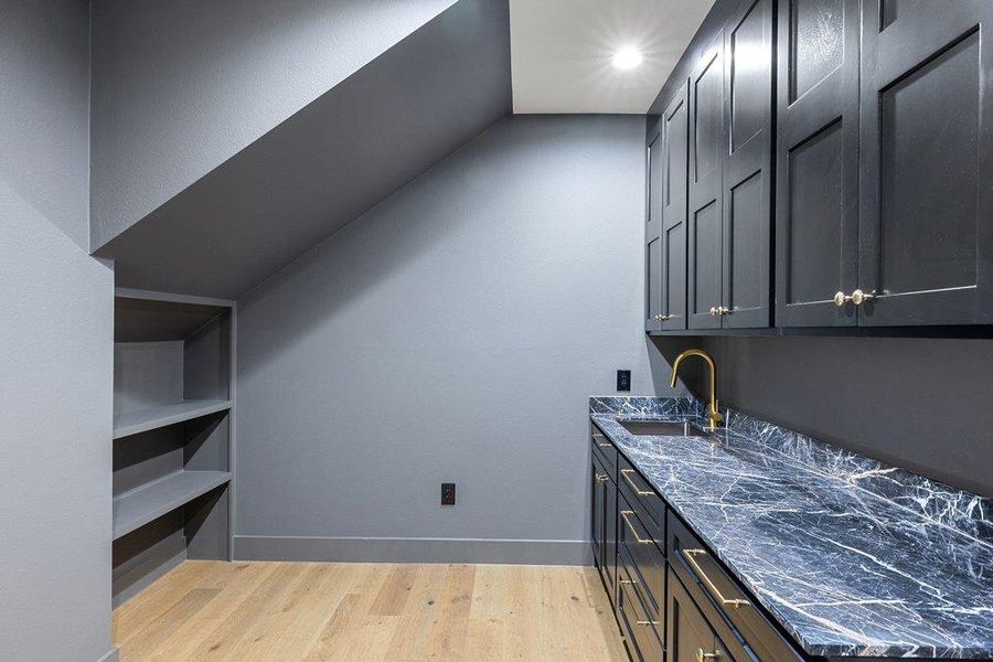 A well-appointed wet bar with marble counters, gold fixtures, and ample cabinetry provides sophisticated entertaining space.