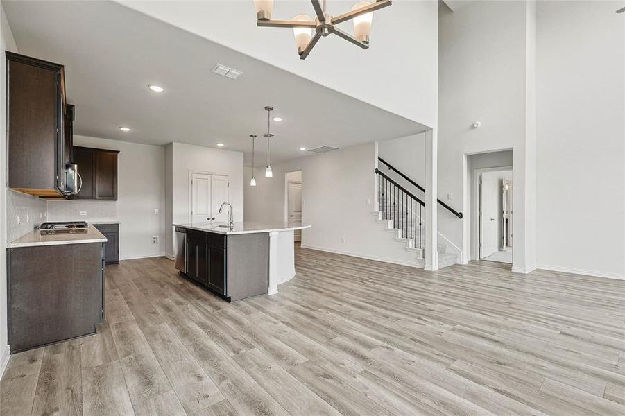 Kitchen featuring tasteful backsplash, hanging light fixtures, an island with sink, sink, and light hardwood / wood-style floors