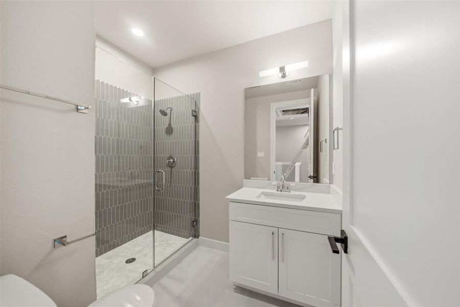 This modern bathroom features a sleek glass-enclosed shower with stylish gray tiling, a white vanity with a contemporary sink, and bright lighting, creating a clean and inviting space.