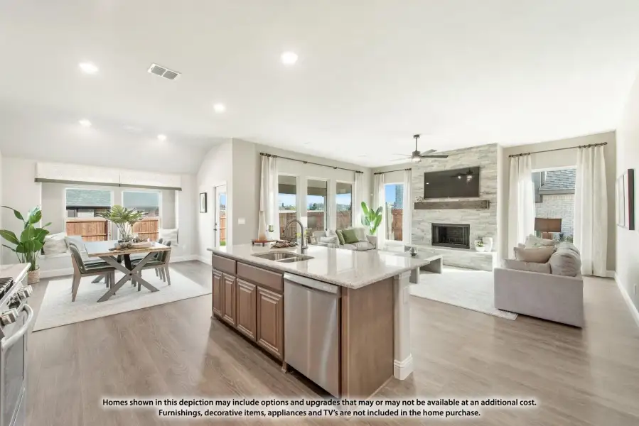 Open-concept kitchen with island flowing into dining and living areas with stone fireplace and hardwood floors