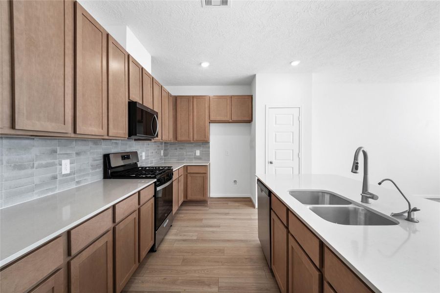 The kitchen features high ceilings, stained wood cabinets, Silestone countertops, SS appliances including microwave, modern tile backsplash, recessed lighting, huge kitchen island extended for a breakfast bar, and a pantry all overlooking your huge Great Room.