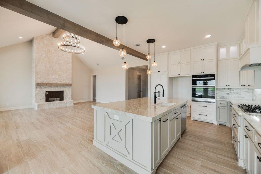Kitchen with an island with sink, light wood-type flooring, a stone fireplace, and backsplash