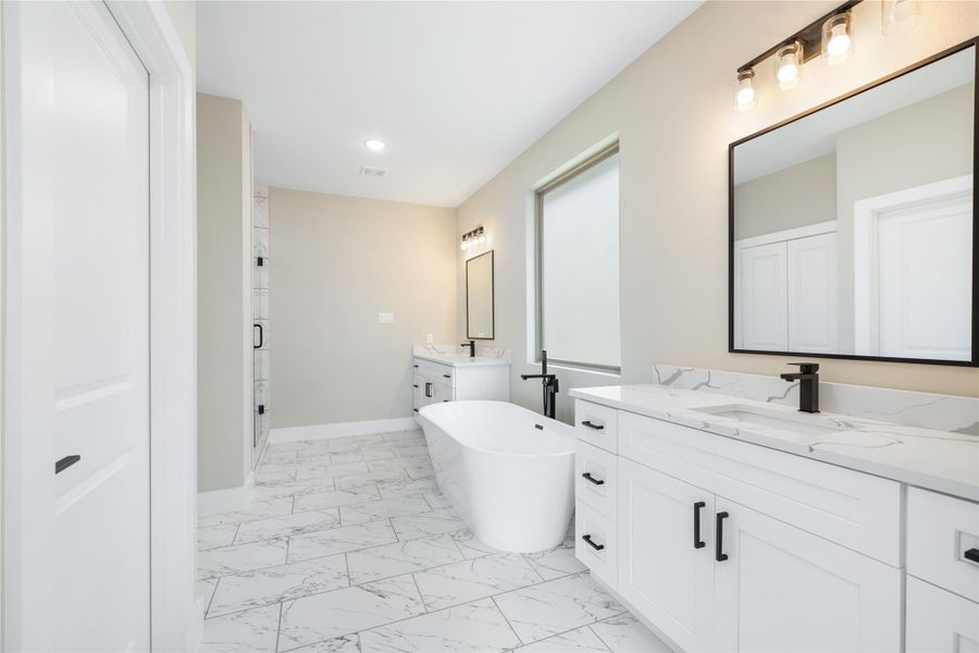 The expansive primary bathroom offers a sleek, modern design with a luxurious freestanding soaking tub, featuring a pure white finish accented by bold black details.