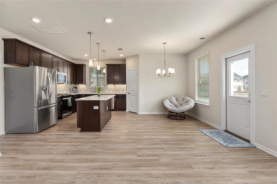 Kitchen with dark brown cabinets, appliances with stainless steel finishes, a center island, decorative backsplash, and hanging light fixtures